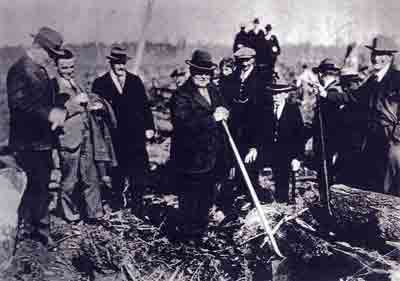 Photo: John W. Berry, MLS, planting tree No. 2 in the Inaugural Plantation, March 15, 1930. Others, left-right: Colonel Nelson Spencer, young Tom Berry, MLA Mike Manson, Peter Z. Caverhill (Chief Engineer), and Ed Walmsley (Land Agent), resting foot on log.